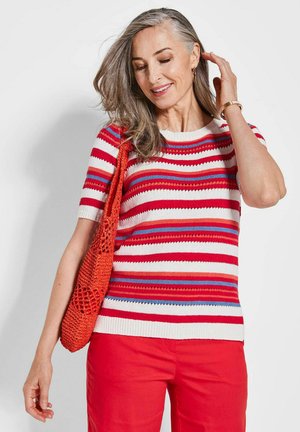 Pull en tricot rayé rouge, blanc et bleu, à manches courtes et col rond, associé à un pantalon rouge vif et un sac orange texturé.