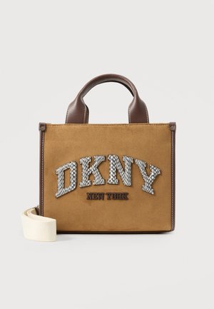 Brun ruskind- og lædertaske fra DKNY New York med top-håndtag og aftagelig hvid rem på ensfarvet baggrund.