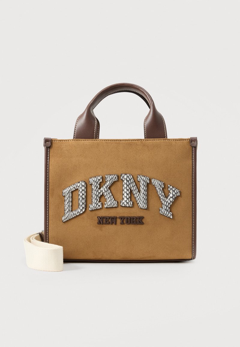 Καφέ τσάντα DKNY New York από σουέτ και δέρμα με πάνω χερούλια και αποσπώμενο λευκό λουράκι σε μονόχρωμο φόντο.