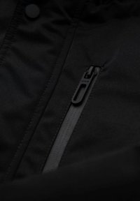 Chaqueta de tela negra con un bolsillo diagonal con cremallera fina y texturizada, y broches planos en la parte delantera.