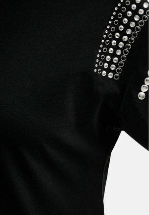 Tessuto nero con borchie decorative argentate disposte in motivi verticali e circolari vicino all'area della spalla di un indumento.