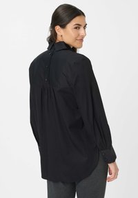 Camicia nera con colletto, design con pieghe sul retro e maniche lunghe. Presenta bottoni neri lungo il retro e sui polsini. Tessuto morbido.