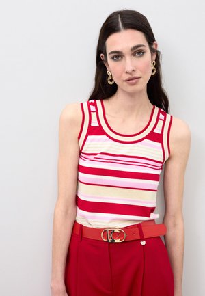 Gestreept mouwloos topje in rood, roze en crème met een ronde halslijn. Draagt bijpassende roodkleurige hoge taillebroeken en een bijpassende riem. Gouden oorringen.