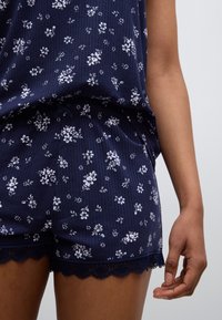 Ensemble de nuit bleu marine à motif floral, texture côtelée, bordure en dentelle sur le short, tissu léger, conçu pour le confort et la détente.