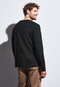 Camisa negra de manga larga hecha de algodón, con cuello redondo y un corte relajado. La camisa tiene una textura suave y un dobladillo recto.