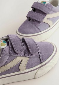 Paarse suede sneakers met witte rubberen zolen en klittenband. Kenmerken een beige accent en een kleurrijke logo-label. Textuur van het bovenmateriaal.