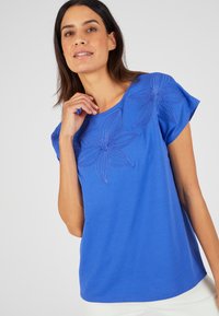 T-shirt di cotone blu con maniche corte, caratterizzato da ricami floreali sulla parte superiore anteriore, texture liscia e scollo rotondo.