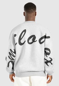 Sweatshirt gris avec du texte cursif noir dans le dos et sur les manches, doté de poignets et d'un ourlet côtelés pour un ajustement élégant.