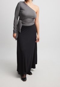 Haut gris à une épaule avec une manche longue, détail de taille nouée ; associé à une longue jupe noire. Texture lisse et silhouette fluide.