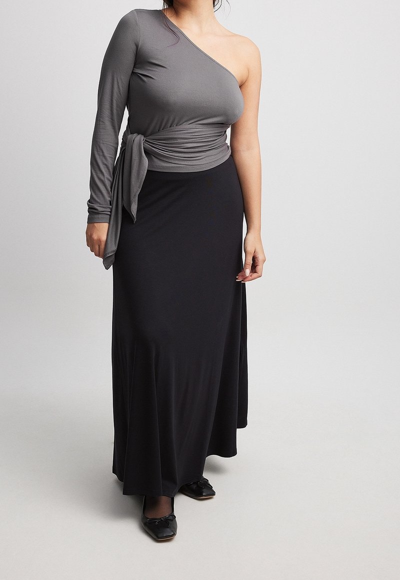 Haut gris à une épaule avec une manche longue, détail de taille nouée ; associé à une longue jupe noire. Texture lisse et silhouette fluide.