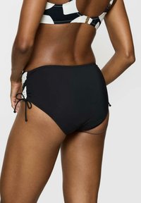 Czarne kostiumy kąpielowe z wysokim stanem, z bocznymi marszczeniami i regulowanymi wiązaniami, w połączeniu z wzorzystym biustonoszem bikini.