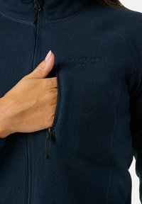 Marine fleece jack met hoge kraag. Voorzien van een ritszak op de borst, textuurstof en een tonale logo op de bovenste linkerkant.