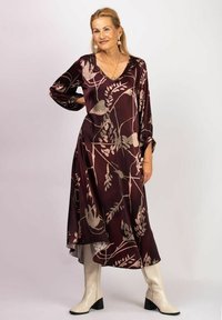 Flytande burgundy klänning med bruna blommönster, V-ringning, långa ärmar och asymmetrisk fåll, med knähöga krämfärgade stövlar.