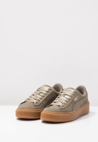 Baskets en daim beige avec lacets métalliques, semelle extérieure en gomme caoutchouc et côtés texturés. Présentent une silhouette classique basse et un logo distinctif.