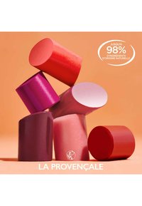 Groupe de six produits pour les lèvres en forme de cylindre, d'une variété de teintes de rouge, rose et violet, avec des finitions brillantes et mates sur un fond orange.