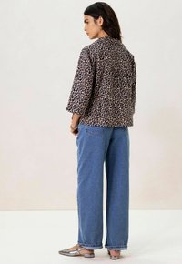 Veste à manches courtes en léopard avec une coupe décontractée, associée à un jean bleu clair à jambes larges et à des ballerines métalliques argentées. Design simple et texture douce.