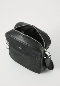Borsa a tracolla in pelle nera texture con zip argentata, grande tasca frontale e manico regolabile. Presenta un dettagli logo minimalista.