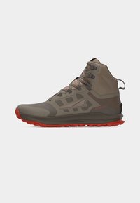 Υψηλό αδιάβροχο μποτάκι πεζοπορίας σε καφέ με κόκκινη σόλα, εμπρόσθιους κορδονιές και επένδυση υποστήριξης αστραγάλου, φαίνεται από το πλάι.