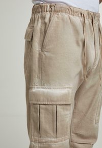 Beige cargo-housut, joissa on joustava vyötärö, sivutaskut ja teksturoitu kangas. Ominaisuuksiin kuuluvat näkyvät saumat ja kaksinkertaiset etutaskut.