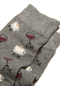 Grå sokker med gentagne mønstre af kaffekopper mærket "AM" og vinglas mærket "PM" på en hvid baggrund.