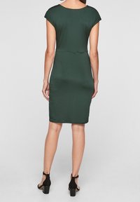 Grön figursydd klänning med korta ärmar, knädlång nederkant, mjuk textur, med en enkel design och i kombination med svarta högklackade sandaler.