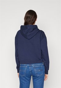 Felpa cropped blu navy con cappuccio regolabile, vestibilità comoda e polsini a costine, abbinata a jeans in denim blu chiaro.