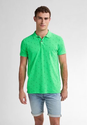 Polo vert avec de petits accents à motifs, en coton, doté d'un col et de manches courtes, associé à un short en denim clair.
