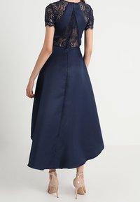 Marineblauw jurk met een kanten lijfje en korte mouwen, voorzien van een uitlopende satijnen rok en een sleutelgatdetail aan de achterkant.