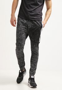 Černé jogger kalhoty s acid-wash efektom, těsným střihem, strukturální tkaninou, kontrastními bočními pruhy a akcentovanými švy.