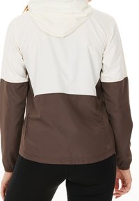 Veste à capuche présentant un design en coloris bloc en crème et marron, fabriquée en tissu léger avec une texture douce et des poignets élastiques.