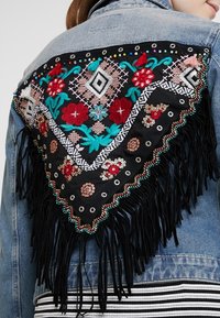 Jeansjacka med en svart, fransad broderad baksida med blommönster, geometriska former och färgglada pärlutsmyckningar.