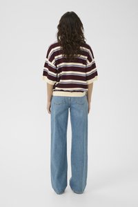Striped pullover in maroon, cream, and blue, paired with loose-fitting light blue jeans. Crew neck, short sleeves, relaxed silhouette.