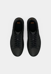 Sorte skinnsko med glatt finish, med sorte lisser, oransje logo og subtile sideaksenter. Klassisk lavt design.