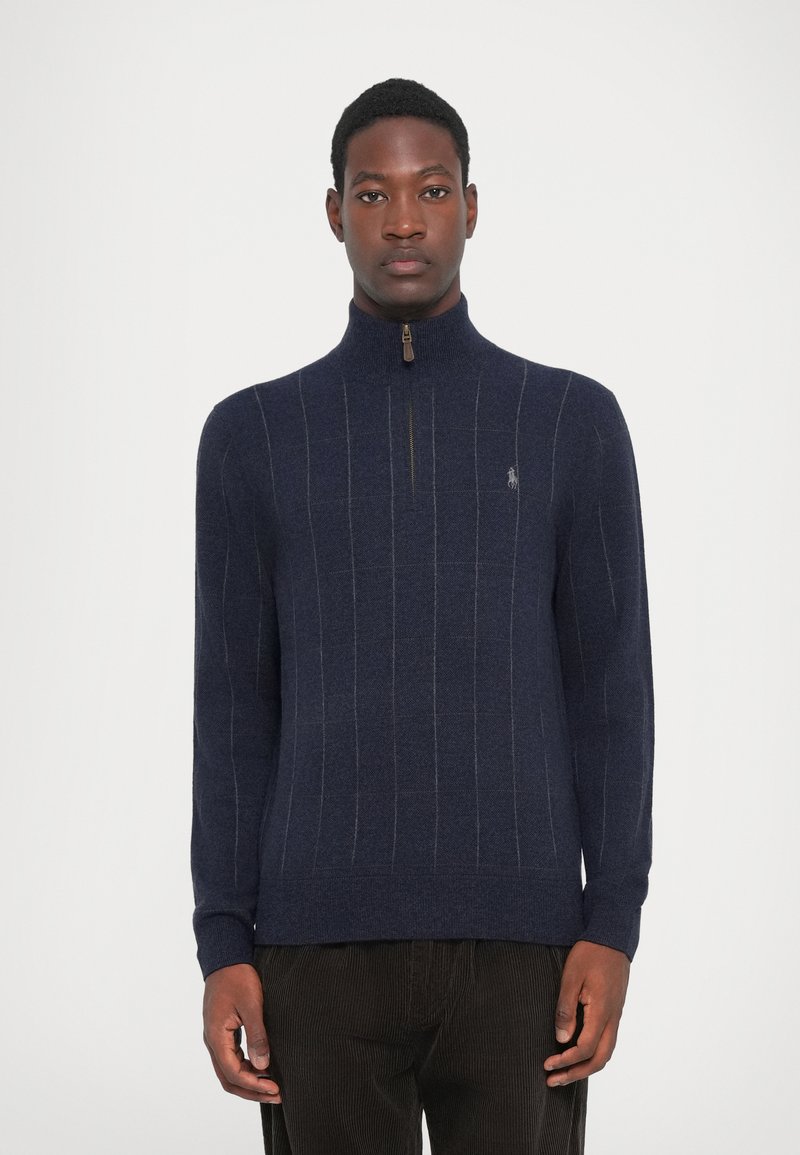Granatowy sweter z zamkiem pod szyją wykonany z dzianiny w pionowe paski. Posiada stojący kołnierz oraz ściągacze przy mankietach. Logo na piersi.