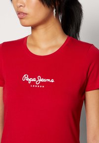 T-shirt rossa in cotone con scollatura tonda, caratterizzata da testo bianco "Pepe Jeans London". Maniche corte e design aderente.
