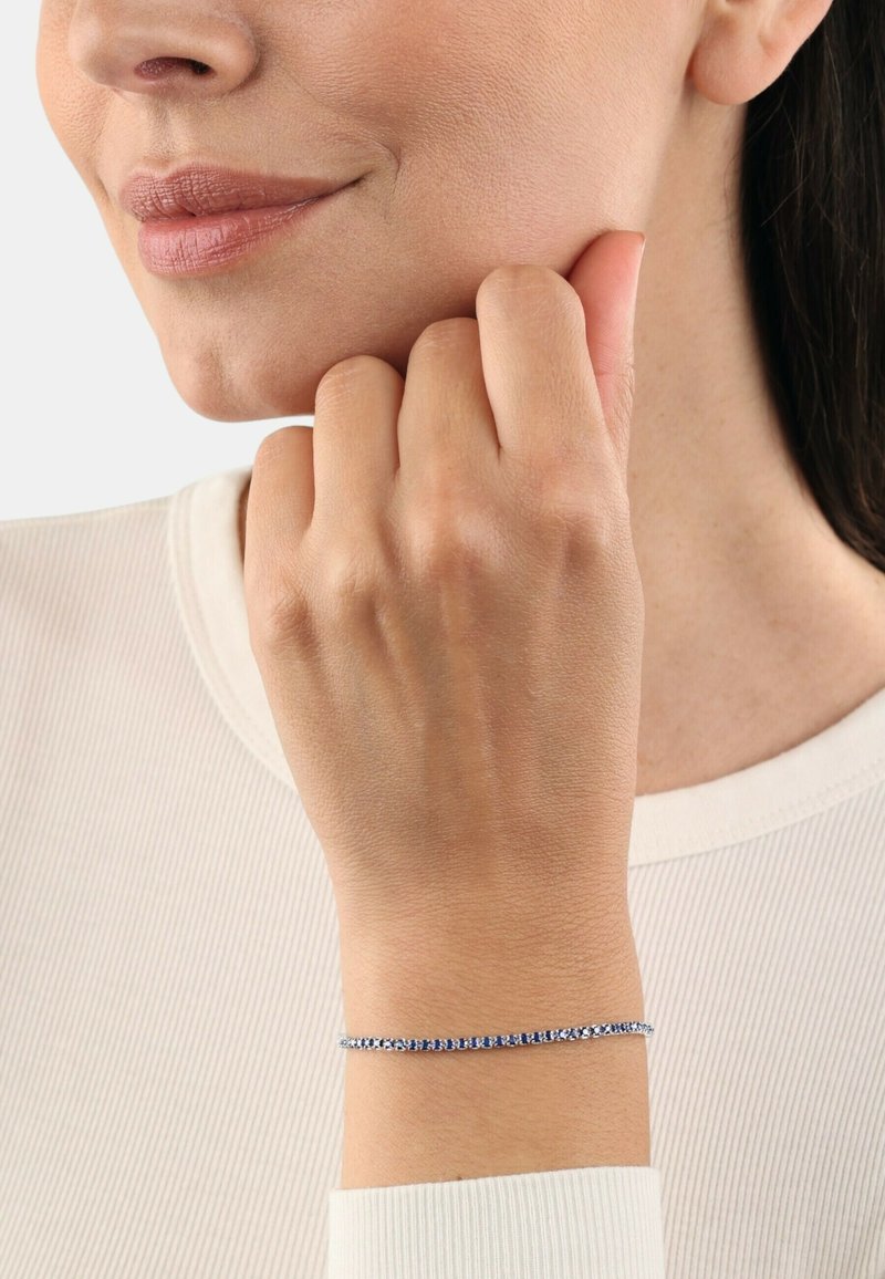 Pulsera de plata con piedras preciosas azules, que presenta un diseño delicado y esbelto que se envuelve alrededor de la muñeca, sobre un fondo claro.