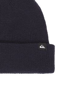 Námorně modrý pletený čepice s ohrnutým okrajem, s malou černobílou štítkovou nálepkou na boku. Texturovaná, elastická látka.