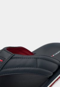 Σκούρο μπλε σαγιονάρα με υφασμάτινο συνθετικό επάνω μέρος με υφή, κόκκινη εσωτερική επένδυση και λευκή σόλα. Διαθέτει ραμμένο λουράκι με λογότυπα.