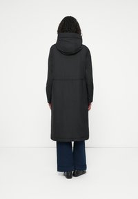 Zwarte hoodie lange jas met een tailleband, een gladde textuur en licht uitlopende mouwen, gecombineerd met wijde blauwe denim broek.