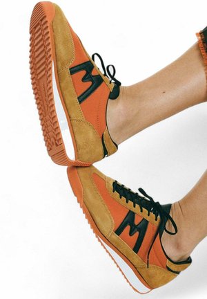 Oranje en beige suède sneakers met zwarte accenten en veters. Dikke rubberen zool met uitgesproken profielpatroon. Ontwerp met afgeronde neus.