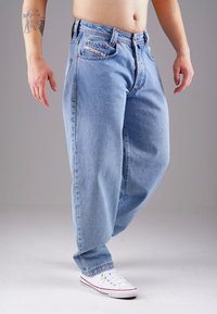 Light blue denim jeans with a relaxed fit, featuring copper rivets, five pockets, and a faded texture. Worn with white sneakers.