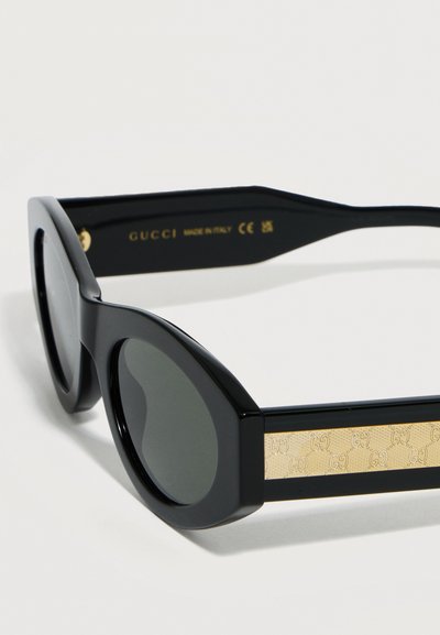 Γυναικεία γυαλιά ηλίου με μαύρους φακούς σε σχήμα γάτας, με διακοσμητικό χρυσό λογότυπο Gucci στα πλαινά και την επιγραφή "Made in Italy" στο εσωτερικό του βραχίονα.