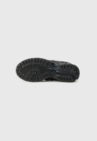 Black athletic shoe sole with textured rubber tread, featuring various geometric patterns and deep grooves for traction.