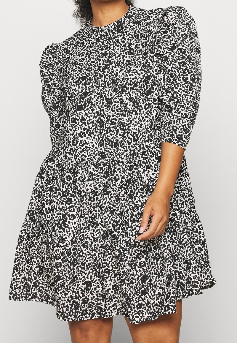 Femme portant une robe noire et blanche à imprimé animalier, avec des manches trois-quarts bouffantes et une jupe évasée.