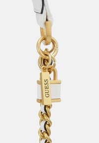 Cintura in pelle bianca con hardware dorato, inclusi un lucchetto e dettagli in catena. Presenta un logo "GUESS" su un'etichetta rettangolare dorata.