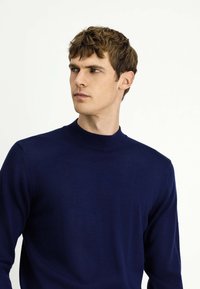 Granatowy sweter dzianinowy z wysokim okrągłym dekoltem, miękką teksturą i długimi rękawami. Tkanina wydaje się gładka, bez widocznych wzorów ani akcentów.