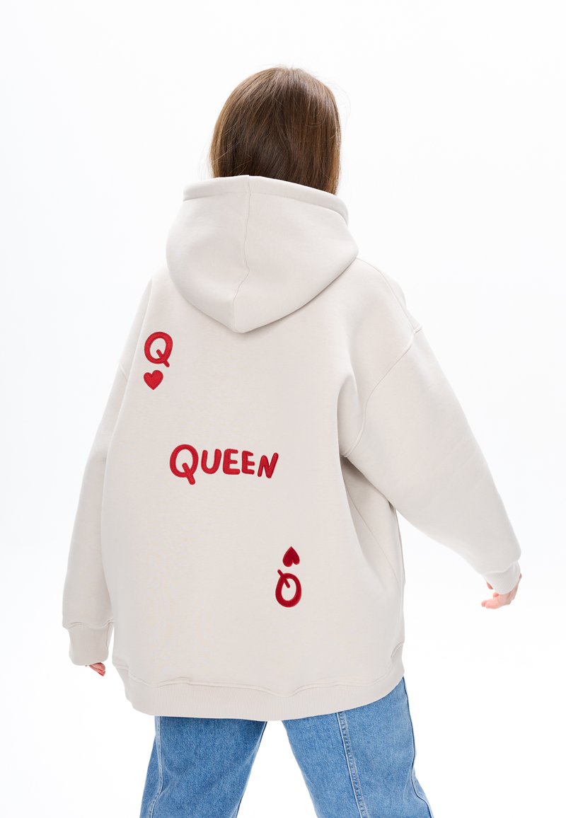 Helle beiga, oversized Kapuzenpullover mit rohem gestickten Text "QUEEN" und dekorativen Elementen wie einem Herzen und einem Ring. Weicher Stoff.