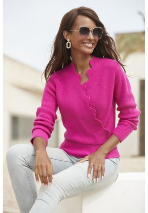 Fuchsia gestrickter Pullover mit gewelltem Ausschnitt und gerippten Bündchen, kombiniert mit hellblauen Jeans. Angenehme Textur, lässige Passform.