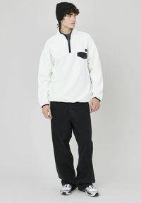 Pull en polaire blanche avec un zip sur le devant, poche poitrine noire et accents noirs. Associé à un jean noir ample et des baskets.
