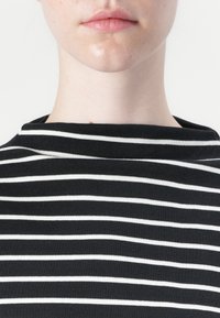 Top riscado em preto e branco com decote redondo, apresentando riscas finas e uniformemente espaçadas. O tecido parece suave e ligeiramente elástico.